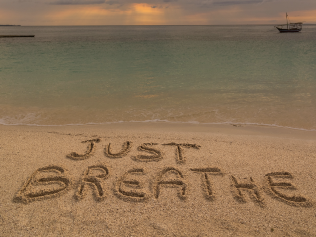 "just breathe" written in the sand on the beach